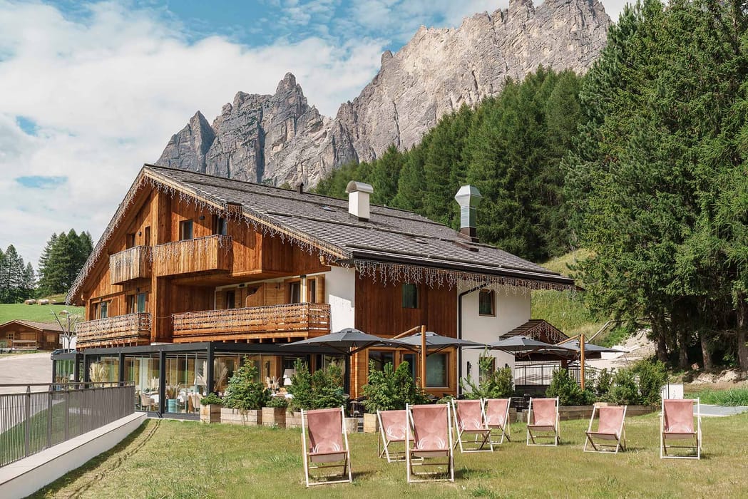 Facciata esterna Casa Guargnè Cortina d’Ampezzo durante l'estate con prato verde e sdraio